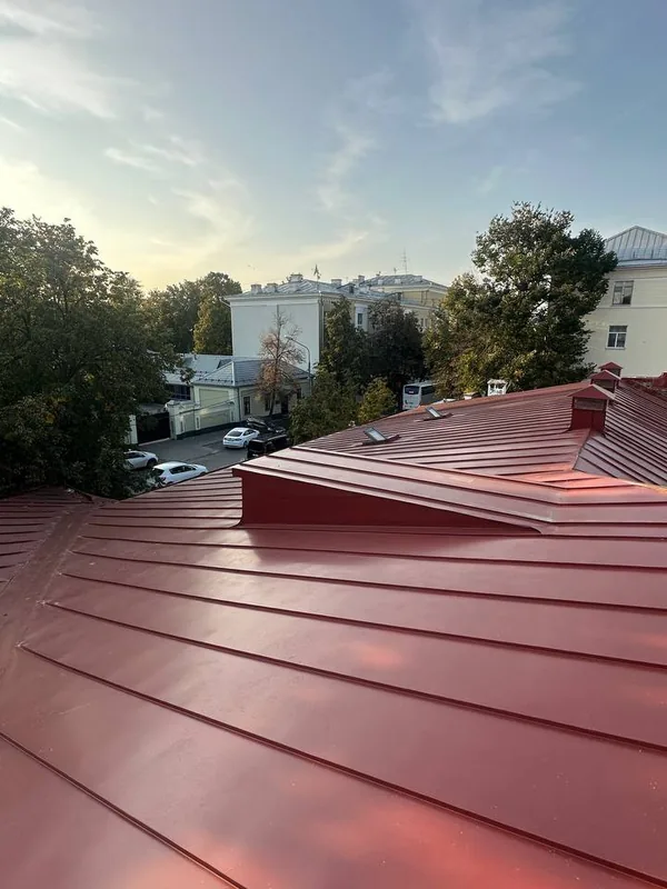 Фальцевая кровля сложной формы в тёплом терракотовом цвете на городском объекте с мансардными выходами и видом на застройку